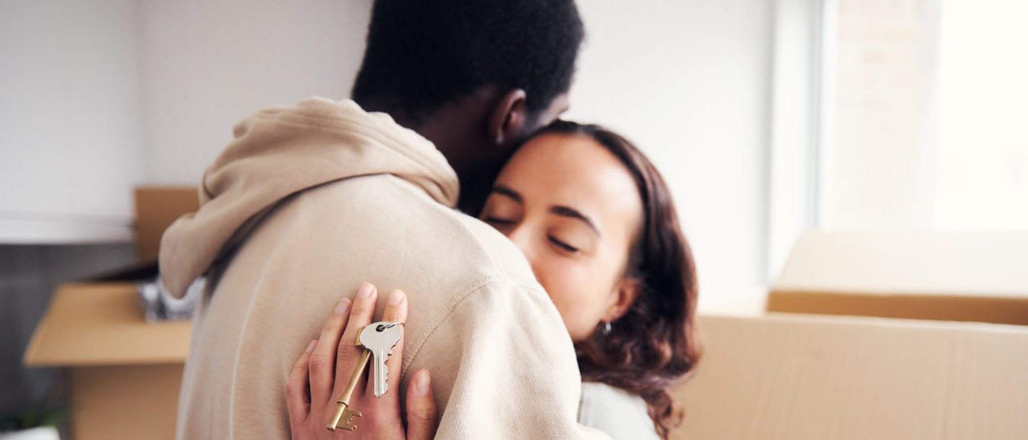 A couple embraces after receiving the keys to their new home, with moving boxes behind them.