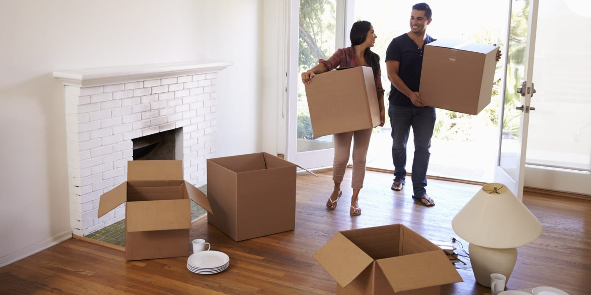A couple carries moving boxes into a bright, airy foyer of their new home.