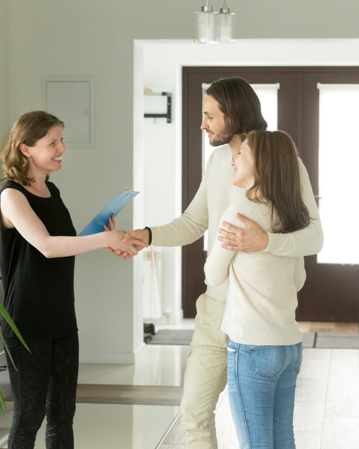 A real estate agent shakes hands with a homebuyer couple in a bright home entryway